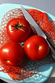 Drei Tomaten mit Messer auf einem Netz