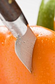 Messer steckt in oranger Paprikaschote