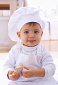 Little girl in chef's hat eating biscuit