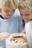 Two boys looking at chocolate chip cookies in biscuit tin