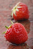 Two strawberries on wet brick background