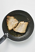 Two fried fish fillets in frying pan