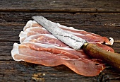 Slices of Parma ham with old knife on wooden background