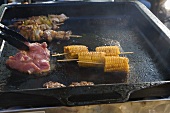 Corn on the cob, steak and kebabs in a grill pan
