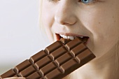 Mädchen beisst in eine Tafel Vollmilchschokolade