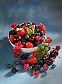 Mixed berries and cherries in and in front of bowl