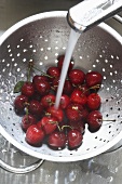 Washing cherries in a colander under running water