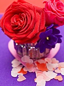 Red roses and African violets in vase, paper hearts