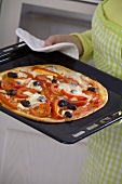 Woman holding red pepper pizza on baking tray
