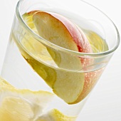 Ein Glas Wasser mit Zitronenschnitz und Apfelspalte