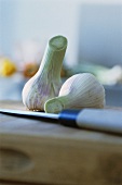 Two fresh garlic bulbs on chopping board with knife