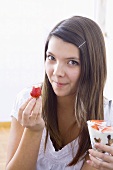 Girl holding yoghurt muesli and bitten strawberry