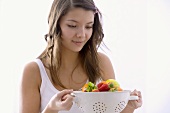Girl holding a kitchen sieve with fresh fruit