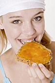 Junge Frau beißt in Brot mit Aprikosenmarmelade