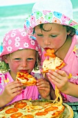 Two children eating pizza on the beach
