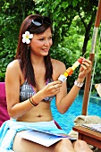 Woman on lounger by pool with fruit skewer