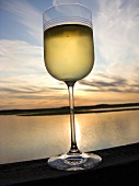 Weissweinglas vor Sonnenuntergang am Meer