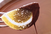 Kandierte Zitronenscheibe auf Gabel, in Schokosauce getaucht