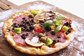 Pizza topped with salami, mushrooms, olives & basil