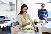 Young couple in kitchen, woman preparing salad