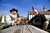 Mann mit Irokesenschnitt und Mann in bayerischer Tracht im Biergarten
