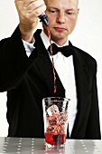 Barkeeper giesst rote Flüssigkeit in Cocktailglas