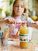 Girl decorating a bottle of apple juice