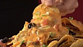 Hand taking nacho with melted cheese from plate