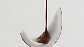 Pouring chocolate sauce over a piece of coconut