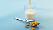 A spoonful of cornflakes and a glass of milk being poured