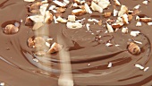 Haselnüsse fallen in flüssige Schokolade
