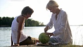 Zwei Frauen schneiden eine Wassermelone beim Picknick