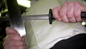 Koch schärft ein Küchenmesser mit dem Wetzstahl