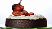 Putting cream and strawberry slices on chocolate cake