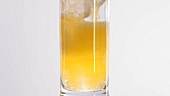 Pouring orangeade into a glass containing ice cubes