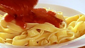 Putting ribbon pasta and tomato sauce on a plate