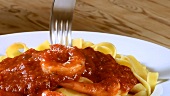 Wrapping ribbon pasta with tomato sauce and prawns round fork