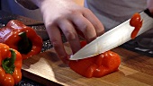 Eine frische, rote Paprika in Streifen schneiden