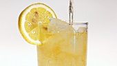 Pouring apple juice into a glass of crushed ice with a slice of lemon