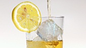 Pouring apple juice into a glass of ice cubes with a slice of lemon