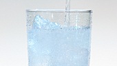 Pouring mineral water into a glass of ice cubes (close-up)