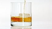 Pouring whisky into a glass with one ice cube