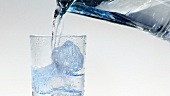 Wasser aus der Kanne in ein Glas mit Eiswürfeln gießen