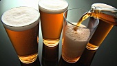 Ale, three full glasses and a glass being poured
