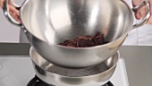 Placing a bowl of chocolate coating over a pan of simmering water