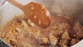 Stirring beef goulash with a wooden spoon