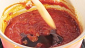 Dark syrup being stirred into barbecue sauce