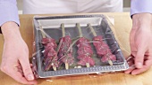 Marinated lamb kebabs being covered with cling film