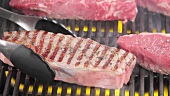 New York strip steaks being turned on a grill