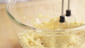 Biscuit dough being mixed with a hand mixer and eggs being added